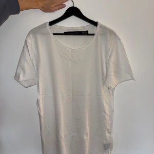 Vit t-shirt från The Black Label Collection - Vit t-shirt i klassisk modell från The Black Label Collection. T-shirten har rund halsringning och korta ärmar, tillverkad i mjuk bomull som känns skön mot huden. Perfekt basic-plagg med clean look och neutral färg, enkel att matcha med allt.