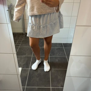 Blommig ljusblå volangkjol - Supersöt kort kjol i ljusblått med små vita blommor och volangdetaljer. Kjolen har resår i midjan för skön passform och är gjord i mjuk bomull. Perfekt för dig som gillar romantisk och chill stil med lite extra volym.💞