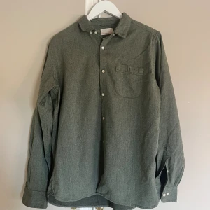 Grön skjorta Knowledge Cotton Apparel - Snygg grön skjorta från Knowledge Cotton Apparel i storlek L. Skjortan har klassisk krage, bröstficka och vita knappar framtill. Materialet är mjuk bomull och passformen är normal. Perfekt att styla med jeans eller chinos för en chill look.