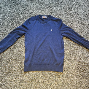 Marinblå merinoulltröja från Morris - Snygg marinblå tröja från Morris i 100% merinoull. Klassisk rund halsringning, långärmad och med diskret broderad logga på bröstet. Perfekt för dig som gillar stilrena och bekväma plagg med premiumkänsla.