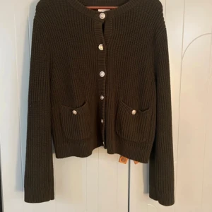 Mörkgrön stickad kofta från H&M - Mysig mörkgrön stickad kofta från H&M med snygga guldknappar framtill och två små fickor. Koftan har långärmad passform och är ribbstickad. 