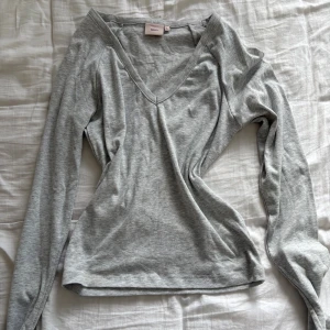 Grå v-ringad långärmad tröja Nelly - Snygg grå långärmad tröja från Nelly med v-ringning. Enkel och stilren modell i mjuk bomull, perfekt att matcha med jeans eller kjol. Passar dig som gillar basic men ändå vill ha en snygg detalj med v-ringad hals.