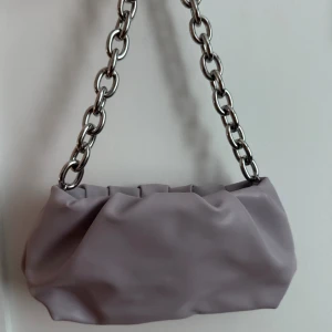 Ljuslila axelväska från H&M - Snygg ljuslila axelväska från H&M med chunky silverfärgad kedja som axelrem. Väskan är gjord i mjukt syntetmaterial och har ett rymligt fack med dragkedja. Perfekt för att lyfta din outfit med en cool detalj. Inga defekter.