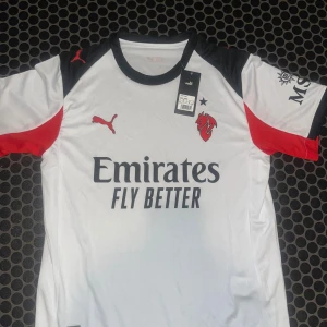 AC Milan vit bortatröja Puma - AC Milan bortatröja från Puma i vitt med svarta och röda detaljer. Tröjan har korta ärmar, svart krage och är tillverkad i tekniskt funktionsmaterial (Drycell). Tryck med Emirates Fly Better och klubbmärke på bröstet. Perfekt för fotbollsfans. Bara höra av er vid frågor/funderingar Fraktar samma dag som köp🚚