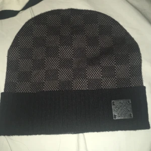  rutig svart mössa - Exklusiv svart mössa med klassiskt rutigt mönster och ribbad. Perfekt accessoar för dig som vill ha en lyxig och stilren look.