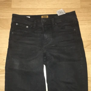 Svarta slim jeans från Jack & Jones - Svarta jeans från Jack & Jones i modellen Slim Glenn. Klassisk femficksdesign med smal passform och normal midja. Jeansen är tillverkade i ett mjukt bomullsmaterial med stretch för extra komfort. Perfekt för dig som gillar en stilren och enkel look.