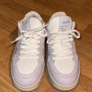 Axel Arigato sneakers i lila och vitt - Snygga sneakers från Axel Arigato, de heter Area Low purple white. Jättesnygga skor som inte kommit till användning utan endast testade. Skorna är i storlek 38 men skulle säga det är en liten storlek och passar 37-37/5. Skolåda medföljer 