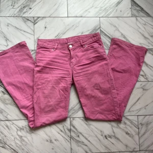 Rosa bootcut jeans med låg midja - Säljer ett par snygga rosa jeans med bootcut-modell och låg midja. Byxorna har klassisk femficksdesign, dragkedja och knapp framtill. Materialet är mjukt och stretchigt bomullstyg som sitter skönt på kroppen. Perfekta för dig som vill sticka ut med färg!