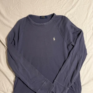 Blå långärmad tröja från Polo Ralph Lauren - Snygg mörkblå långärmad tröja från Polo Ralph Lauren med klassisk rund hals och broderad logga på bröstet. Tillverkad i mjuk bomull som är skön mot huden. Perfekt för dig som gillar stilrena och enkla plagg med en touch av premiumkänsla.