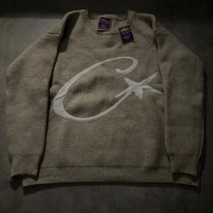 Beige stickad tröja med stjärnmotiv - Säljer en beige stickad tröja från WS i storlek M. Tröjan har ett stort vitt C och en stjärna på framsidan, ribbade muddar vid ärmslut och nederkant samt rund hals. Perfekt för dig som gillar chill och stilren design.