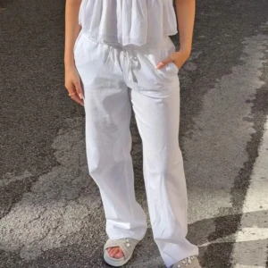 Vita linnebyxor från Gina - Säljer ett par vita linnebyxor med avslappnad passform och snörning i midjan. Byxorna har raka ben och sidfickor, perfekta för varma dagar. Lätta och luftiga, passar dig som gillar en chill och stilren look.