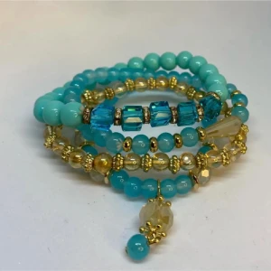 Turkost och guldigt pärlarmband - Flera armband i turkosa och guldiga pärlor med glittrande detaljer och små hängen. Armbanden har både runda och fyrkantiga pärlor i olika nyanser av blått och guld, vilket ger en cool och färgstark look. Ej använd utan kommer från min small business.