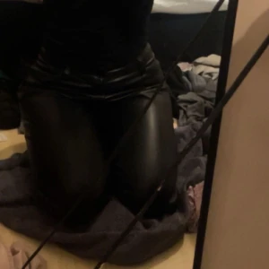 Svarta skinnbyxor med tight passform - Säljer ett par svarta skinnbyxor med snygg, tight passform. Byxorna har klassisk femficksdesign och midja med hällor för bälte. Perfekta för dig som vill ha en edgy look och gillar att sticka ut.