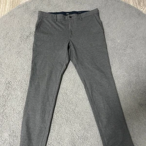 Grå extra slim kostymbyxor från BOSS - Snygga grå kostymbyxor från Hugo Boss i extra slim fit. Byxorna har diskret struktur, klassiska fickor och bälteshällor. Perfekta för dig som gillar en stilren och modern look. Materialet är mjukt och stretchigt för extra komfort.