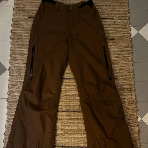Skid byxor - Ljus bruna skid byxor från geotech 6.0 teknologi i xs. Byxorna har fem fickor och luft fickor med blixtlås. Högra benet har några små vita fläckar på sig. Det går också att reglera midjan med kardborre band.
