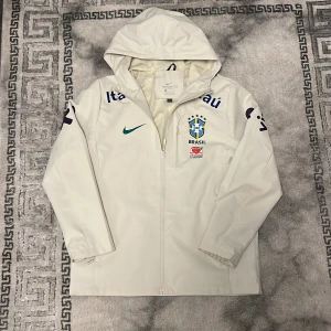 Vit Nike vindjacka med Brazil logga - Vit Nike vindjacka med Brazil-emblem. Storlek XL på etikett men passar mig som vanligtvis har S. Använd ett fåtal gånger, fin kvalité. Pris kan diskuteras. 