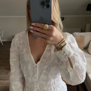 Vit blommig blus med knappar - Säljer en superfin vit blus med blommigt mönster och v-ringning. Blusen har långa ärmar med breda manschetter och dekorativa knappar framtill. Materialet är lätt och ger en romantisk vibe, perfekt till ljusa jeans. Den är figurnära vid midjan och har en feminin siluett. Storlek xs och tröjan är iprincip oanvänd. nypris 400 🤍🥰