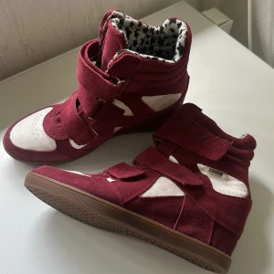 Vinröda sneakers med kardborre från Roots - (8 cm höga) Säljer ett par vinröda sneakers från Roots i mocka och syntet med vita detaljer. Skorna har flera breda kardborreband och en cool innersula med svartvitt stjärnmönster. Brun gummisula och platt sula för skön vardagsstil.