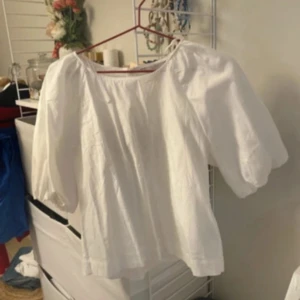 Vit blus med puffärm från H&M - Säljer en vit blus från H&M med puffiga trekvartsärmar och rund halsringning. Blusen är tillverkad i bomull och har en luftig, loose passform som ger en avslappnad och trendig look.