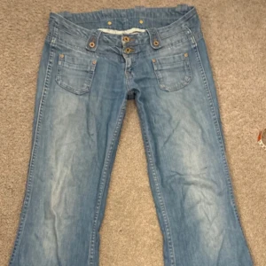 Pepe jeans  ljusblå bootcut  - Säljer ett par ljusblå jeans från Pepe jeans med bootcut passform och väldigt låg midja. Jeansen har flera dekorativa knappar i midjan, klassiska fickor fram och bak samt Pepe -logga på bakfickan. Materialet är mjukt jeans och de har en snygg tvättad look. De är från 2000’s och säljs inte längre. 