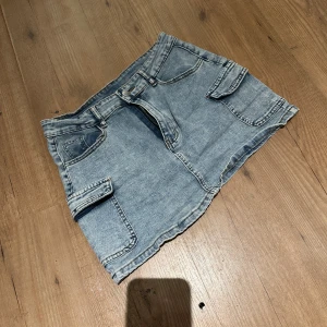 Blå jeanskjol med fickor från SHEIN - Säljer en blå jeanskjol från SHEIN i storlek L. Kjolen är kort och har flera praktiska fickor, både fram och på sidorna, samt hällor för bälte. Den har klassisk jeanslook med knapp och dragkedja framtill. Perfekt för dig som gillar streetstyle och denim. Väldigt stretchig!