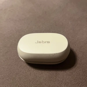 Jabra Elite 75t - Jabra Elite 75t trådlösa hörlurar i beige med laddningsetui. USB-C laddning. Hörlurarna och etuiet har mindre kosmetiska märken men är i gott skick. Perfekt för musik, samtal och träning med bra batteritid och passform. Boxen är sönder men hörlurarna funkar 