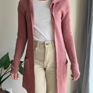 Rosa stickad kofta med huva FB Sister - Mysig lång rosa stickad kofta från FB Sister med huva och två stora fickor framtill. Koftan har ribbad struktur och är perfekt att slänga på sig över en t-shirt. 