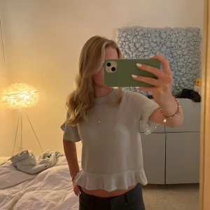 Glittrig silver topp med volangkant - Säljer en glittrig silverfärgad topp med korta ärmar och volangkant nertill. Toppen har en croppad passform och är tillverkad i ett mjukt, glittrande syntetmaterial.