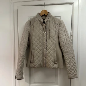 Beige quiltad jacka från Zara  - Beige quiltad jacka från Zara Woman med bruna detaljer och knappar i guld. Storlek M men passar även S. Knappt använd så säljes i mycket fint skick.