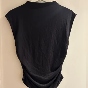 Svart ärmlös topp från Gina Tricot - En svart ärmlös topp från Gina Tricot i mjuk bomull. Toppen har en enkel och stilren design med rund halsringning och något lös passform. Perfekt att styla med jeans eller kjol för en clean look.