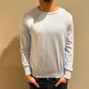 Ljusblå bomullströja med rund hals - En stilren ljusblå tröja från Riley i bomull med rund halsringning och långa ärmar. Tröjan har ribbade muddar vid ärmslut och nederkant för en snygg passform. Perfekt för dig som gillar en clean och enkel look.