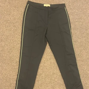 Svarta kostymbyxor med vit rand SELECTED - Svarta kostymbyxor från SELECTED med smal passform och vita ränder längs sidorna. Byxorna har pressveck framtill och diskreta bakfickor. Perfekta för en stilren och trendig look.