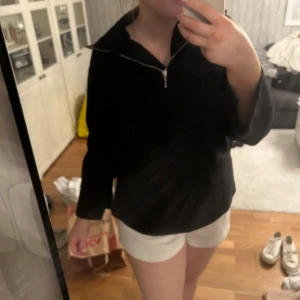 Svart tjocktröja - En svart långärmad tröja. Den är Xs men passar till M oxå. Två slitsar längst ner på sidorna, och slits vid båda ärmslut. En hög krage med dragkedja i fram