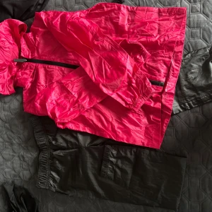 Rosa regnjacka + regnbyxor från Active, stl 134/140 - Säljer en kompakt och lätt rosa regnjacka från Active med svart dragkedja och huva. Jackan är tillverkad i syntetmaterial och har elastiska muddar vid ärmslut. Perfekt att packa med i den medföljande svarta påsen.