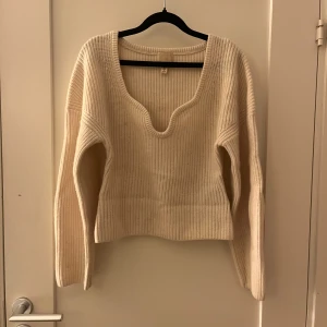 Krämvit stickad tröja från H&M - Säljer en krämvit stickad tröja från H&M i ull. Tröjan har en djup v-ringad hals och ribbad struktur som ger en snygg och modern look. Långärmad och med normal passform, perfekt för att hålla sig varm under kyliga dagar.