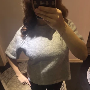 Grå stickad tröja från Gina Tricot - Mysig grå stickad tröja från Gina Tricot med korta ärmar och rund hals. Tröjan har en loose passform och ribbade detaljer vid hals, ärmslut och nederkant. Perfekt för lager-på-lager och chill dagar.