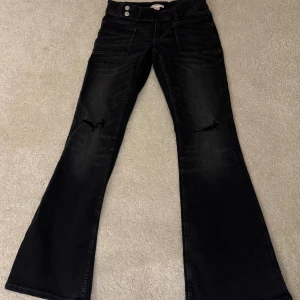 Svarta bootcut jeans Gina Tricot 164 - Svarta jeans från Gina Tricot i storlek 164 med bootcut-ben och slitna detaljer vid knäna. Jeansen har framfickor, dubbla knappar i midjan och klassisk femficksdesign. Perfekta för dig som gillar en trendig och avslappnad look. Dessa är också oanvända därför priset och har aldrig använt dem! 