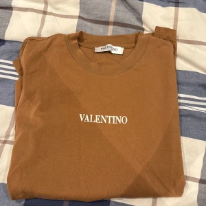 Brun t-shirt från Valentino - Snygg brun t-shirt från Valentino med klassisk rund hals och korta ärmar. T-shirten har en stilren vit logotyp på bröstet och är gjord i mjuk bomull. Perfekt för dig som gillar enkel och clean design med exklusiv känsla.