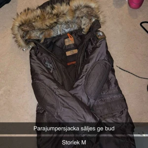 Brun Parajumpers dunjacka med päls - Säljer en brun Parajumpers dunjacka med fluffig päls runt huvan och coola detaljer på ärmarna. Jackan har flera fickor, dragkedja och patch på axeln. Perfekt för dig som vill ha en varm och snygg vinterjacka med street vibe.