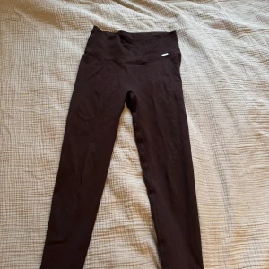 Bruna leggings från Aim'n - Mörkbruna leggings från Aim'n med ribbad midja. Använda fåtal gånger. Tight passform och stretchigt material som sitter skönt. Perfekta för träning eller chill. Hög midja för extra komfort och snygg siluett.