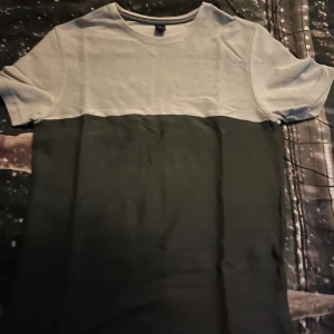 Tvåfärgad t-shirt från Baker's - Snygg t-shirt från Baker's i storlek L med en cool tvådelad design. Övre delen är ljusgrå och nedre delen är svart, vilket ger en stilren kontrast. T-shirten har rund hals och korta ärmar, perfekt för en chill och avslappnad look.