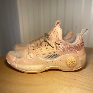 Way Of Wade 10 Low -  Dem är rätt så använda. Säljer ett par snygga sneakers från Li-Ning i en ljus beige färg med inslag av rosa och guldiga detaljer. Skorna har mesh och syntetmaterial, coola detaljer på sidorna och unik sula med cirkulära mönster. Perfekta för dig som gillar sportig och modern stil.