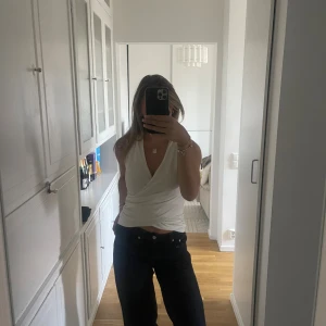 Vit omlott linnetopp med v-ringning - Säljer en vit omlott linnetopp med djup v-ringning och ärmlös design. Toppen har en snygg omlott-detalj framtill och sitter tajt över kroppen. Perfekt till jeans eller kjol för en fräsch och stilren look.