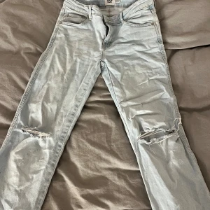 Ljusblå bootcut jeans med slitningar - Säljer ett par ljusblå bootcut jeans från 157 med snygga slitningar på båda knäna. Jeansen har klassisk femficksdesign, dragkedja och knapp framtill. Perfekt för dig som gillar en avslappnad och trendig look.använd 1 gång