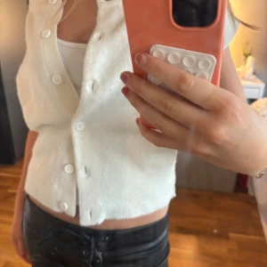 Vit stickad väst från Nelly XS - Superfin vit stickad topp från Nelly i storlek XS. Modellen är croppad med korta ärmar och knappar framtill. Perfekt att styla över ett linne eller t-shirt för en chill look. Mjuk och skön känsla tack vare det stickade materialet.