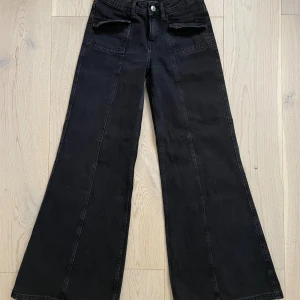 Svarta wide jeans från H&M Divided - Snygga svarta jeans från H&M Divided i storlek 32. Modellen har breda ben och hög midja, med coola fickdetaljer framtill. Materialet är klassisk jeans och färgen är djup svart, perfekt för en trendig look.