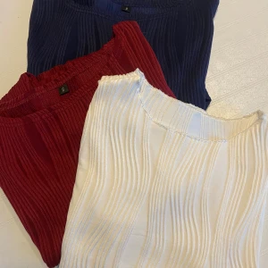 Tre toppar i härliga färger - Säljer 3 ribbstickade toppar storlek S, finns i tre färger: mörkblå, vinröd och vit. Topparna  har ett vågigt ribbmönster. Den vita är kortärmad och de två andra är långärmade. 