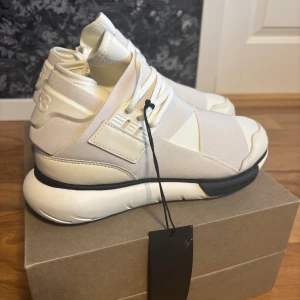 Y-3 Qasa High sneakers i vitt - Säljer ett par Y-3 Qasa High sneakers i vitt med futuristisk design, elastiska band över ovandelen och chunky vit sula. Skorna har detaljer i skinn och textil, snörning och svarta detaljer på sulan med Y-3. Nypris: 8600:- helt nya 