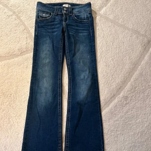 Blå bootcut jeans från Gina Tricot - Snygga blå jeans från Gina Tricot i modell med bootcut. Jeansen har klassisk femficksdesign, dubbla knappar i midjan och kontrastsömmar. Perfekta för dig som gillar en retroinspirerad look med utsvängda ben.