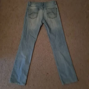 Ljusblå jeans i denim - Säljer ett par ljusblå jeans iklassisk denim med fem fickor och bälteshällor. Dem har en avslappnad passform och snyggt slitna detaljer för en chill vibe.